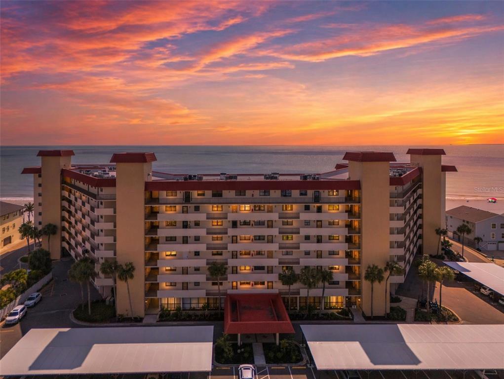 An aerial view of a multi-story beachfront condominium building at sunset with covered parking — 18304 GULF BOULEVARD UNIT 105, REDINGTON SHORES, FL