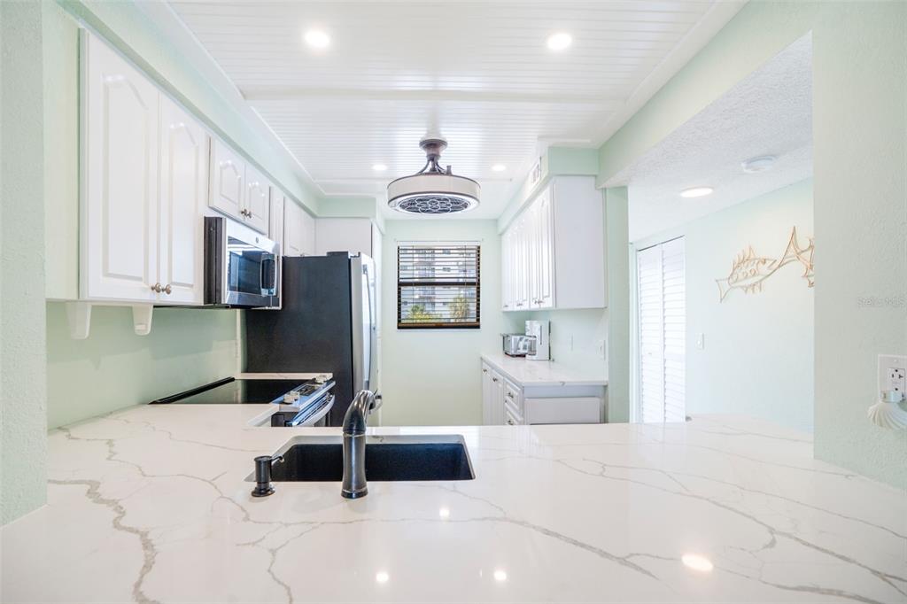 A kitchen features white cabinets, marble-look countertops, a black sink, and a beadboard ceiling — 18304 GULF BOULEVARD UNIT 105, REDINGTON SHORES, FL