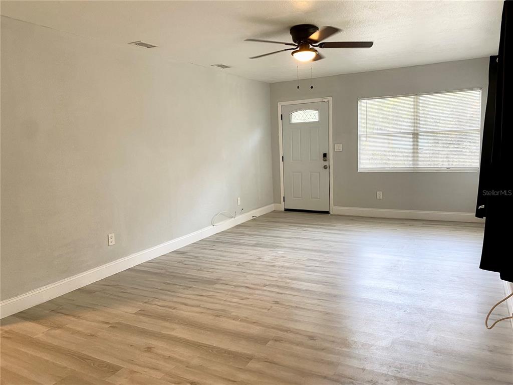 A living room with light-colored wood-look flooring, gray walls, a ceiling fan, and an entry door — 2343 8TH STREET S, ST PETERSBURG, FL