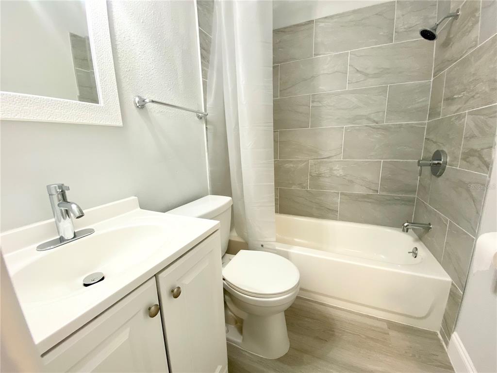 A bathroom features a white vanity, a toilet, and a bathtub with gray tiled walls — 2343 8TH STREET S, ST PETERSBURG, FL