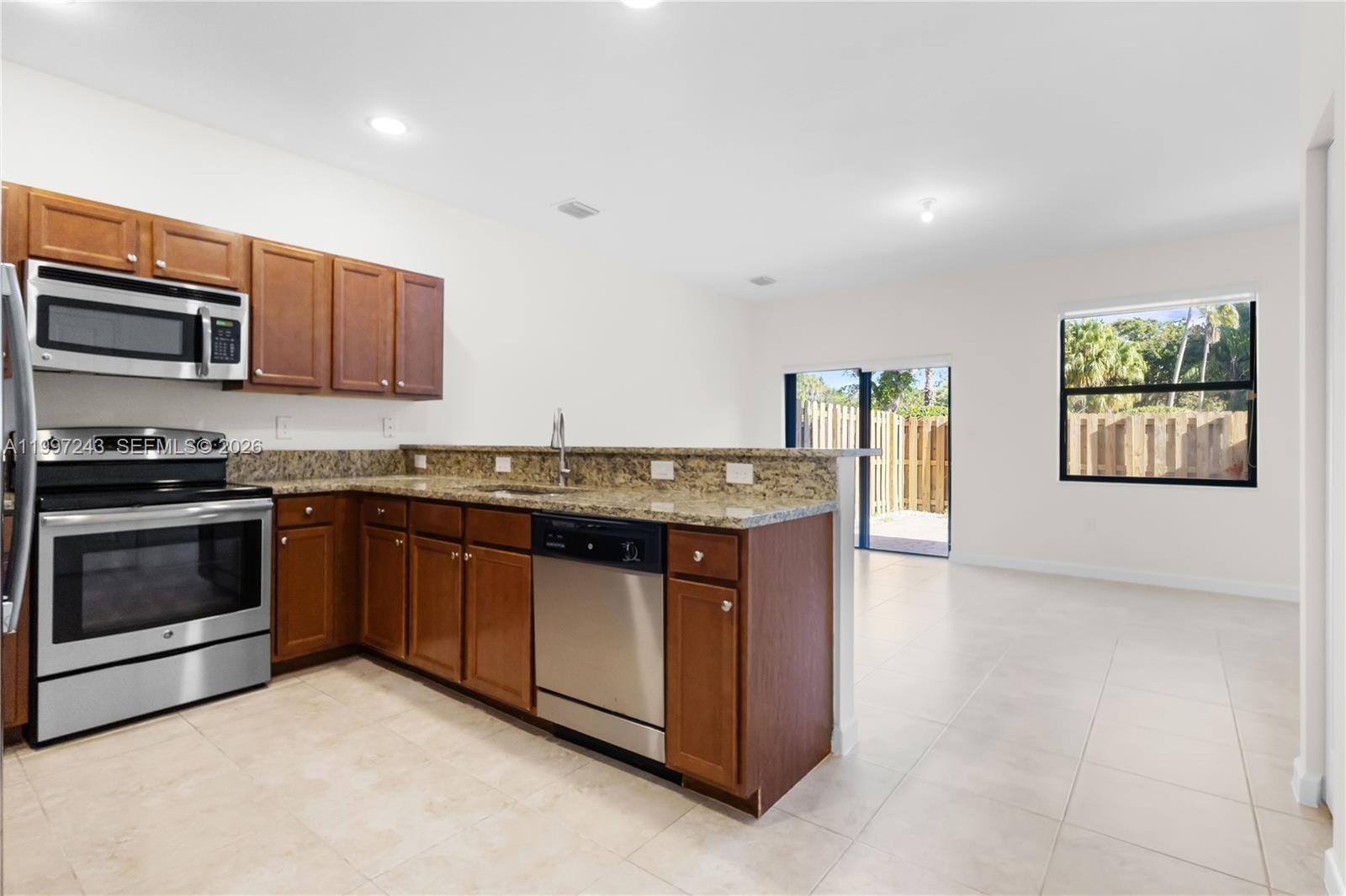 A kitchen with wood cabinets, granite countertops, and stainless steel appliances opens to a living area — 15075 SW 113th Ter, Miami FL 33196, MIAMI, FL