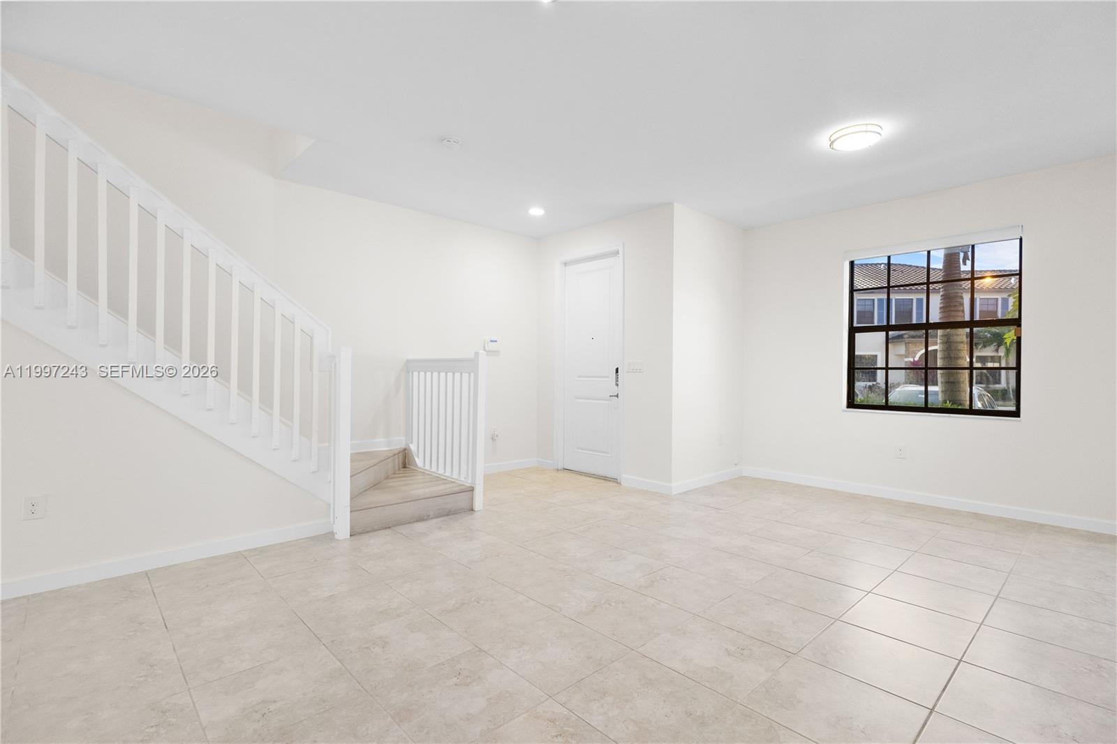 This room features light tile flooring, a white staircase with railings, and a single window — 15075 SW 113th Ter, Miami FL 33196, MIAMI, FL