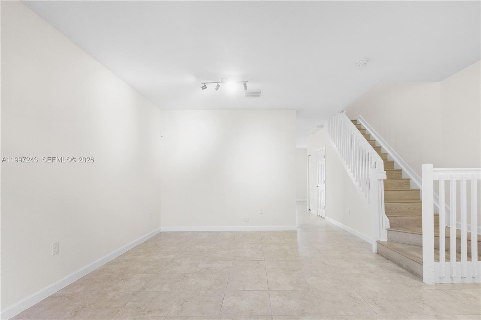 An empty room with tile flooring, white walls, and a staircase with wooden steps — 15075 SW 113th Ter, Miami FL 33196, MIAMI, FL