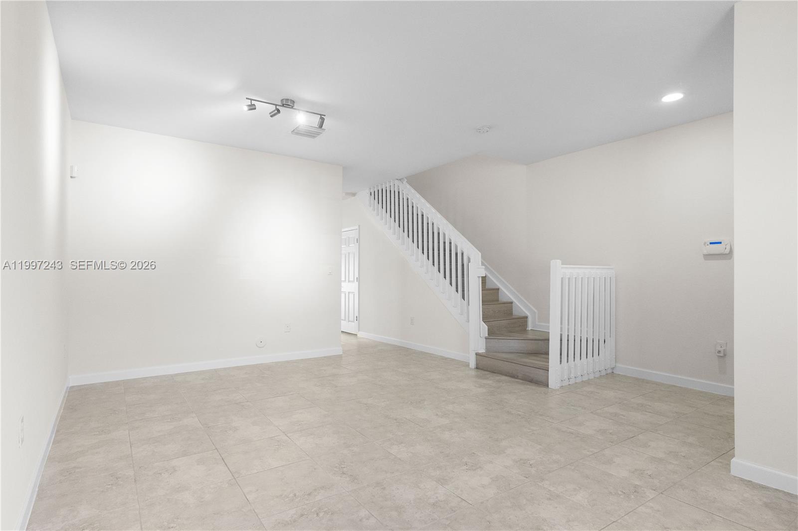 An empty room features light-colored tile flooring, white walls, and a staircase with white railings — 15075 SW 113th Ter, Miami FL 33196, MIAMI, FL