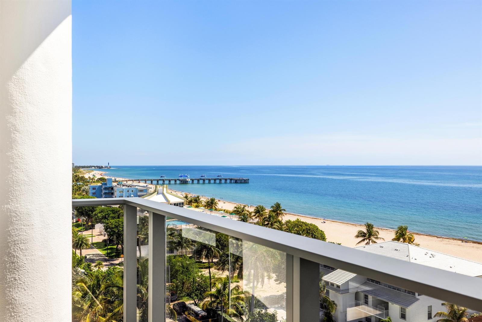 A balcony view overlooking a sandy beach, palm trees, and a pier extending into the ocean — 305 Briny Avenue # 804, Pompano Beach FL 33062, POMPANO BEACH, FL