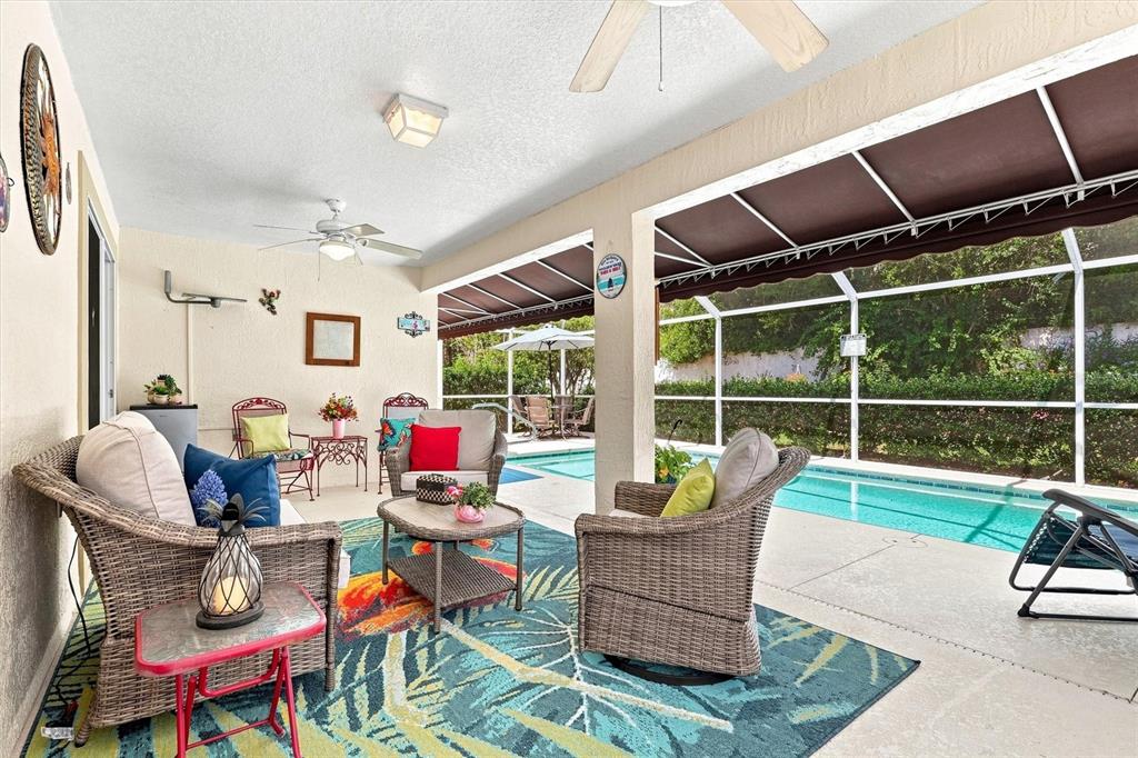 A covered patio features wicker furniture, a colorful area rug, and a screened-in swimming pool — 6133 LANDINGS BOULEVARD, LADY LAKE, FL