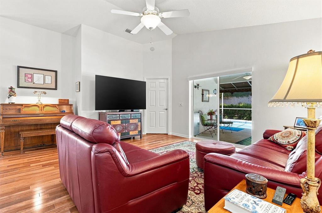 A living room features red leather sofas, a piano, a television, and sliding glass doors — 6133 LANDINGS BOULEVARD, LADY LAKE, FL