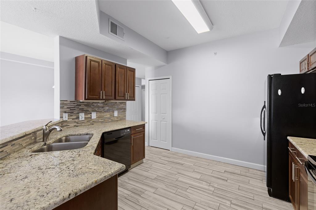 A kitchen features granite countertops, dark wood cabinets, a black dishwasher, and light-colored tile flooring — 6336 BUFORD STREET UNIT 801, ORLANDO, FL