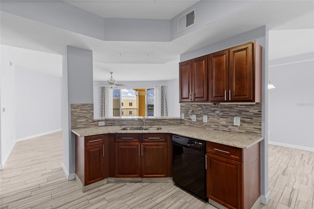 A kitchen with dark wood cabinets, granite countertops, and a tiled backsplash overlooks a balcony — 6336 BUFORD STREET UNIT 801, ORLANDO, FL