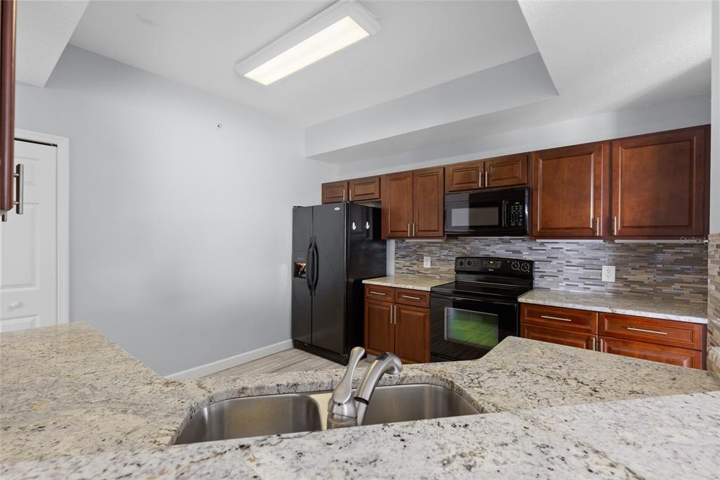 A kitchen features dark wood cabinets, black appliances, granite countertops, and a mosaic tile backsplash — 6336 BUFORD STREET UNIT 801, ORLANDO, FL