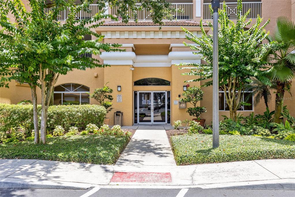 A concrete walkway leads to the glass double-door entrance of a tan multi-story building — 6336 BUFORD STREET UNIT 801, ORLANDO, FL