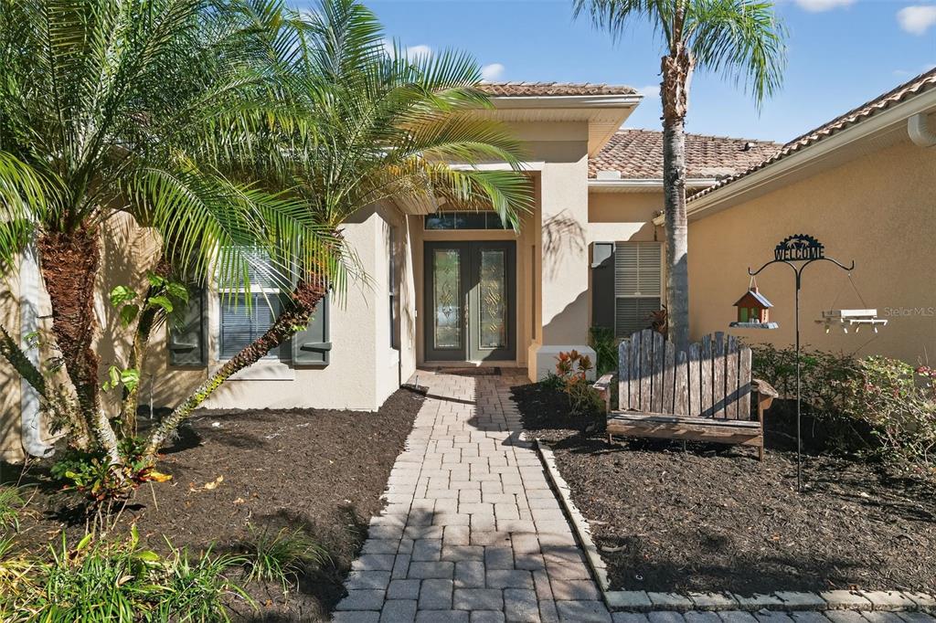 A paved walkway leads to the double front doors of a house with palm trees — 3816 EAGLE ISLE CIRCLE, KISSIMMEE, FL