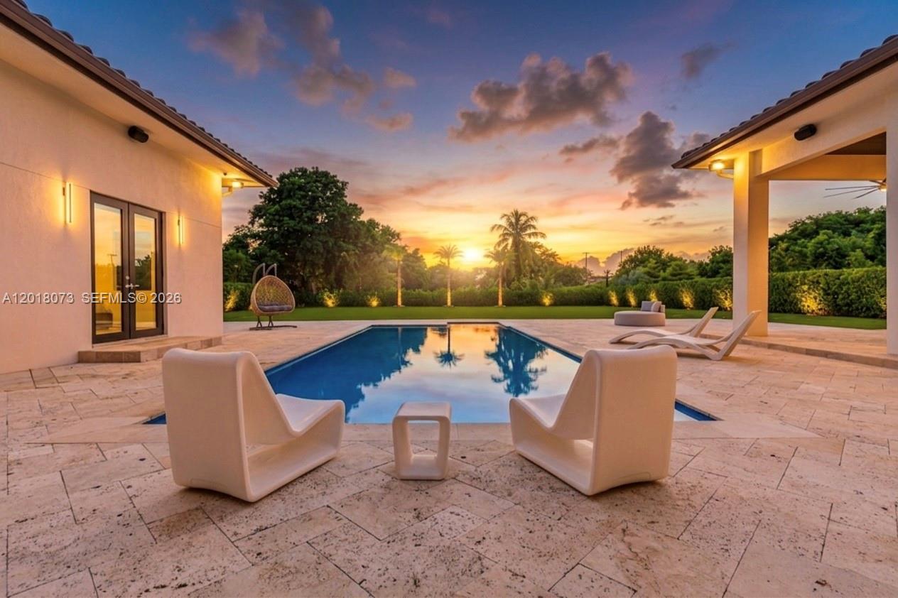 A swimming pool sits on a stone patio between two wings of a house at sunset — 320 SW 125th Ave, Miami FL 33184, MIAMI, FL