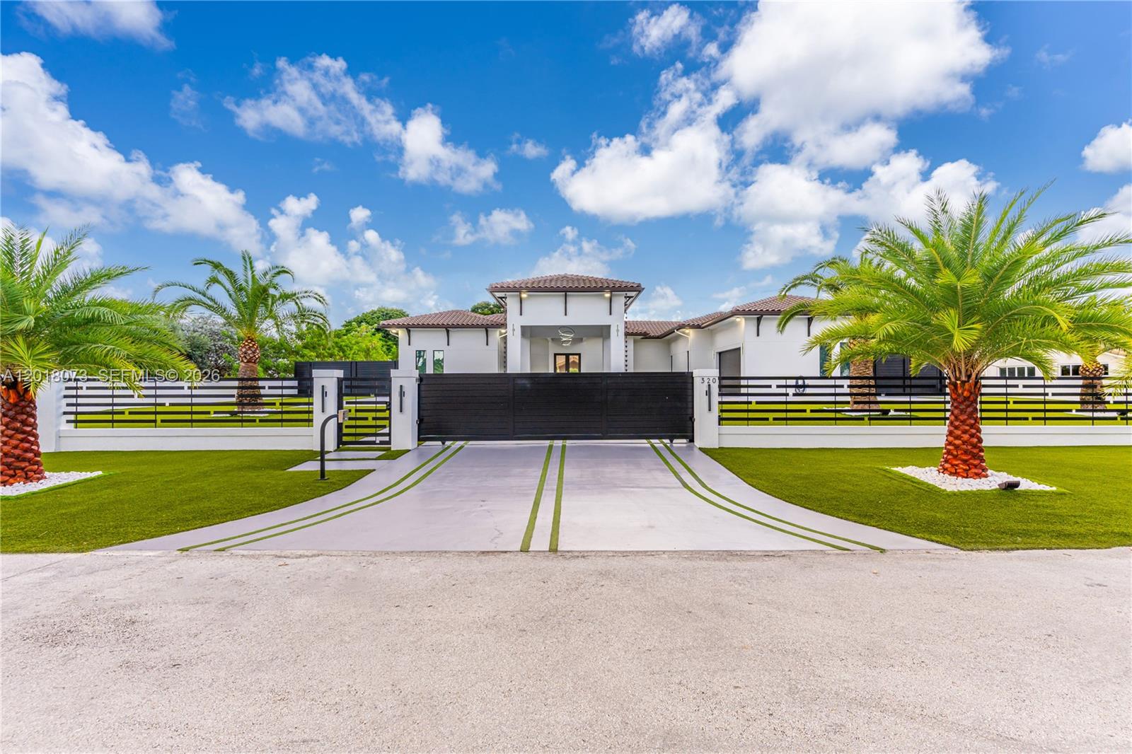A modern white house features a black gated driveway, palm trees, and a manicured lawn — 320 SW 125th Ave, Miami FL 33184, MIAMI, FL