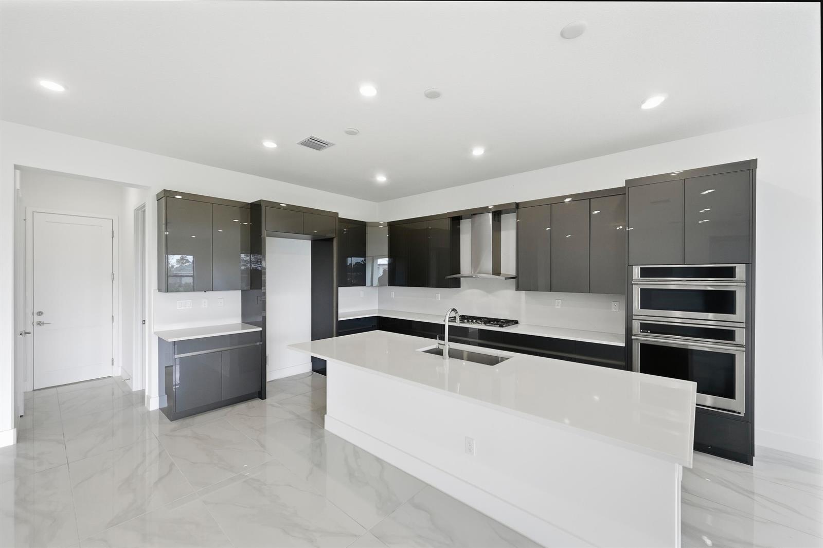 A modern kitchen features glossy gray cabinets, white countertops, a central island, and marble-look flooring — 7593 Bridle Trail Way, Lake Worth FL 33449, LAKE WORTH, FL