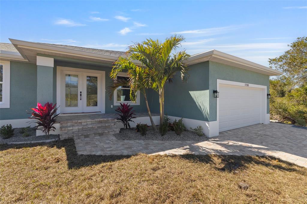 A single-story house with teal stucco walls, a white garage door, and a paved walkway — 17203 CHASE AVENUE, PORT CHARLOTTE, FL