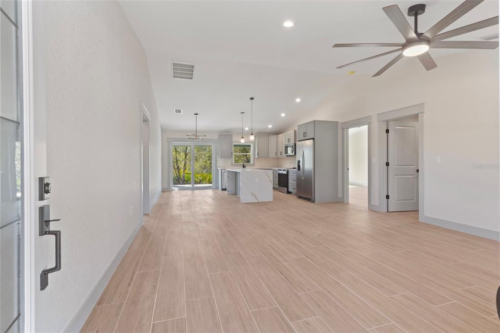 A bright open-concept kitchen and living area features light wood-look tile flooring and gray cabinetry — 17203 CHASE AVENUE, PORT CHARLOTTE, FL