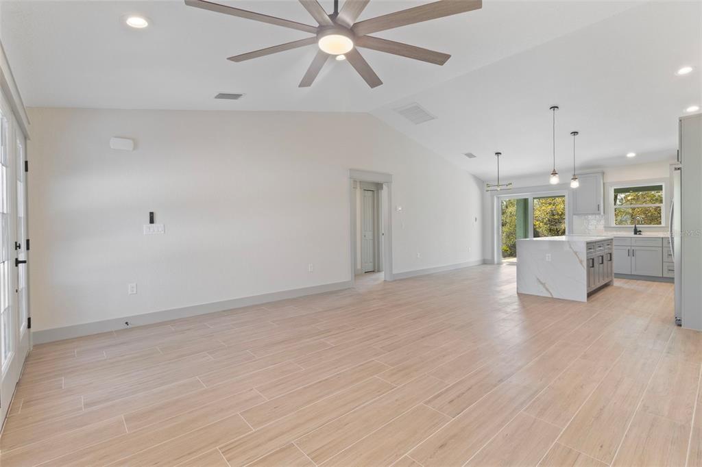 A spacious living area with light wood-look tile floors, a ceiling fan, and an open kitchen — 17203 CHASE AVENUE, PORT CHARLOTTE, FL