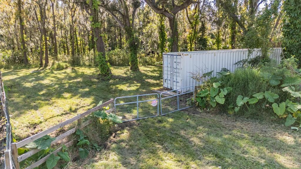 A metal shipping container sits in a grassy, wooded backyard behind a wire farm gate — 18113 672 HIGHWAY, LITHIA, FL