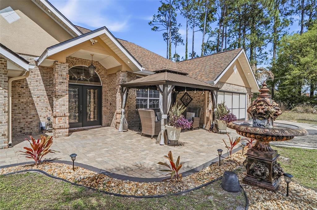 A brick house exterior features a paved patio, a gazebo, and a decorative water fountain — 11 BANNERWOOD LANE, PALM COAST, FL