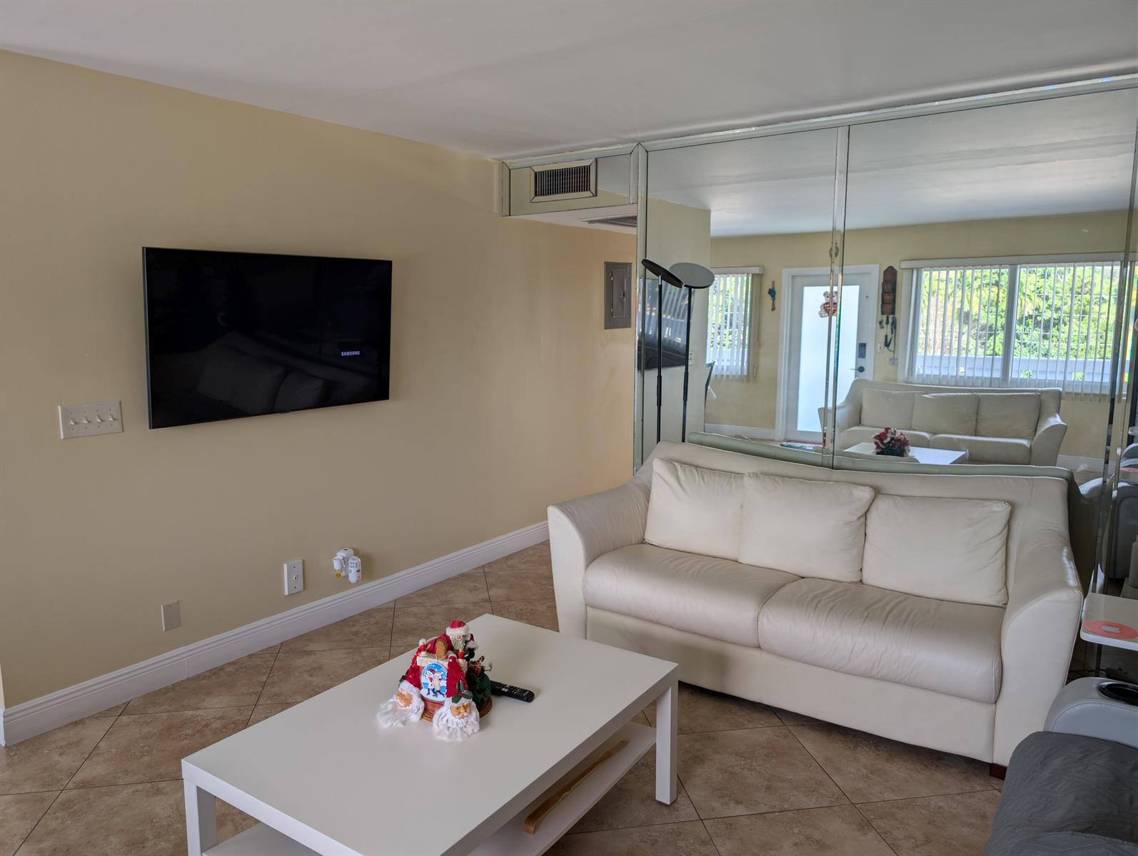 A living room features a wall-mounted television, a white sofa, and a mirrored wall — 3036 Ventnor H # 3036, Deerfield Beach FL 33442, DEERFIELD BEACH, FL