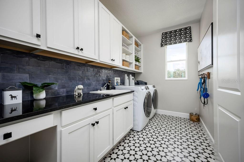 A laundry room features white cabinets, black countertops, blue subway tile, and patterned floor tiles — 3132 SOLACE WAY, ORLANDO, FL
