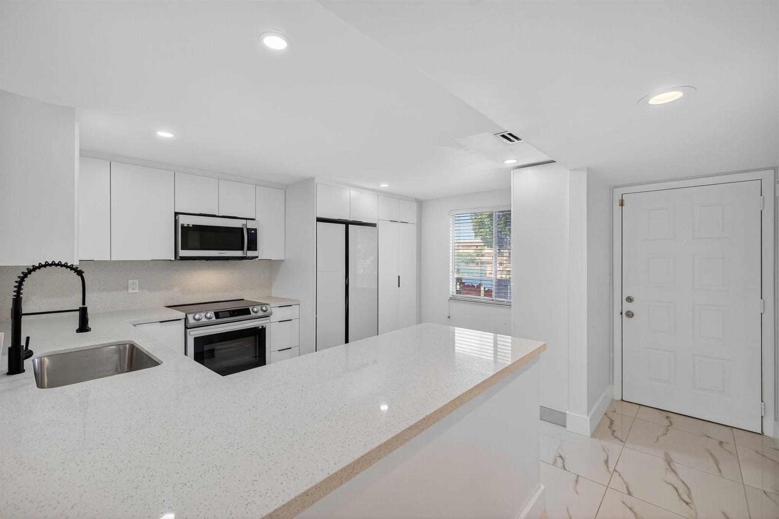 A modern kitchen features white cabinets, quartz countertops, stainless steel appliances, and tile flooring — 14375 Strathmore Lane # 303, Delray Beach FL 33446, DELRAY BEACH, FL