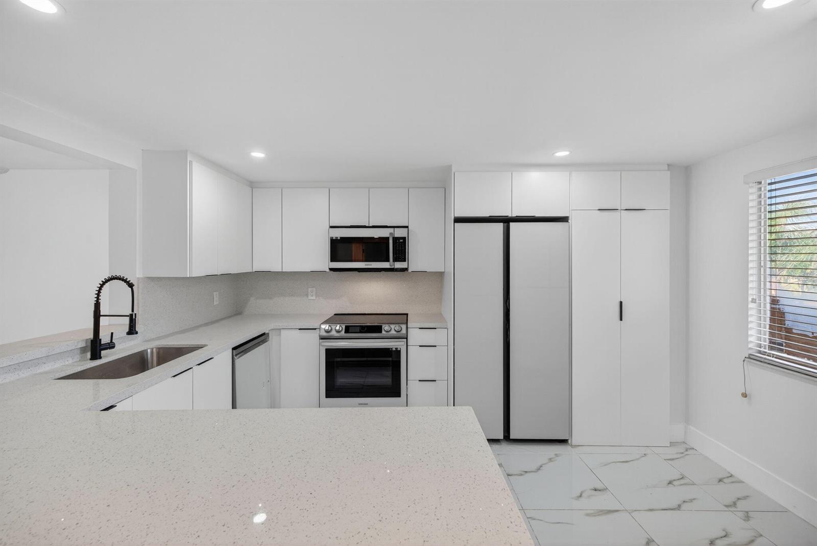 A modern kitchen features white cabinetry, stainless steel appliances, quartz countertops, and marble-look tile flooring — 14375 Strathmore Lane # 303, Delray Beach FL 33446, DELRAY BEACH, FL