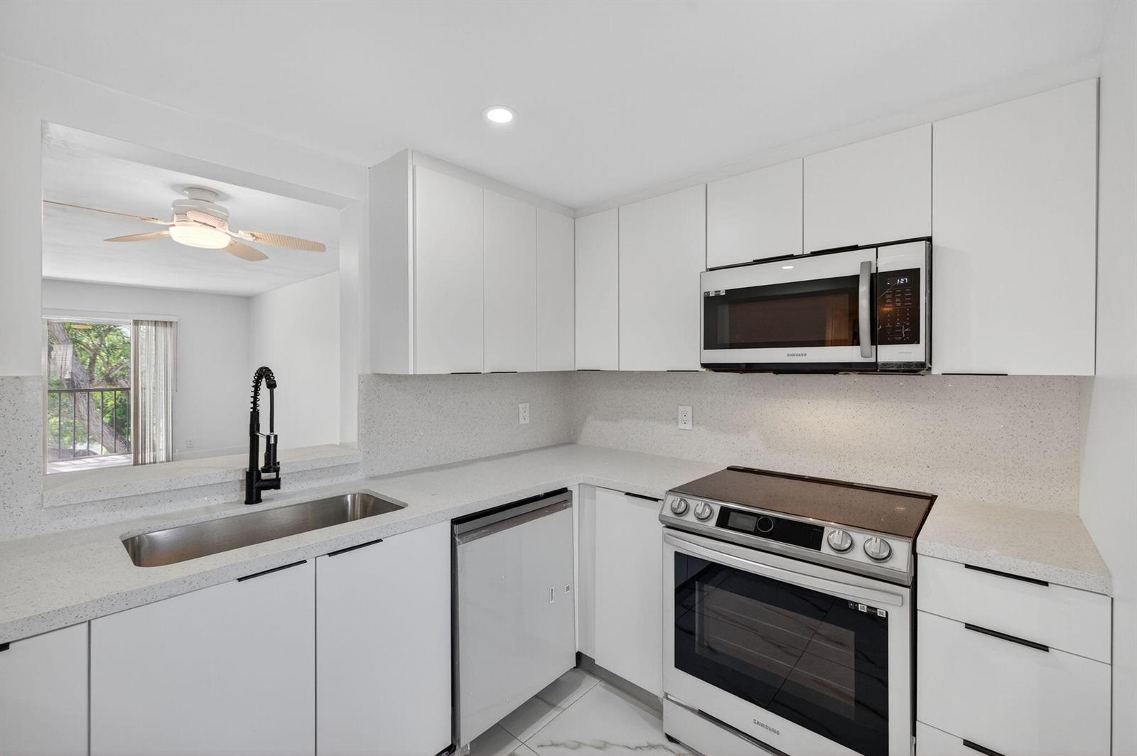 A modern kitchen features white cabinets, quartz countertops, stainless steel appliances, and a pass-through window — 14375 Strathmore Lane # 303, Delray Beach FL 33446, DELRAY BEACH, FL