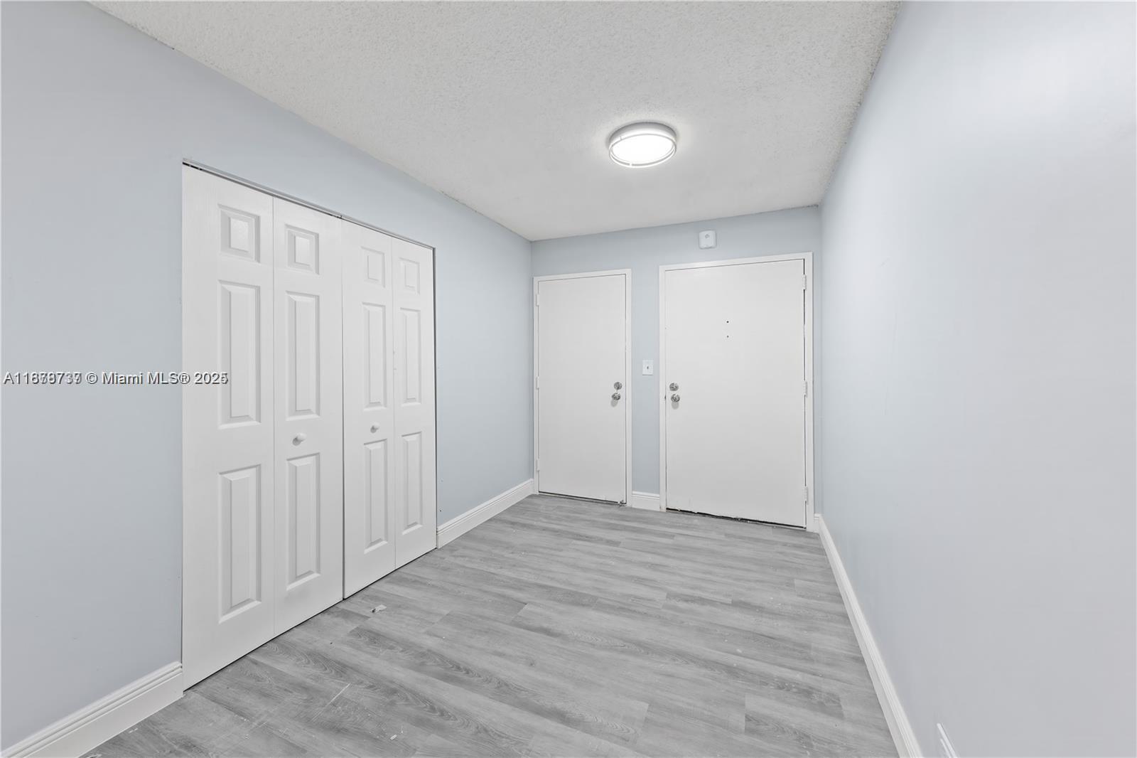A room with light blue walls, gray wood-look flooring, a closet, and two doors — 3680 Inverrary Dr # 3J, Lauderhill FL 33319, LAUDERHILL, FL