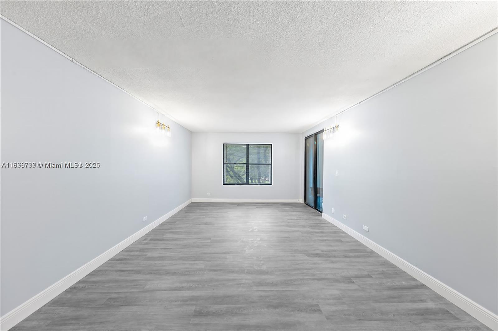 An empty room features light gray walls, wood-look flooring, a central window, and sliding doors — 3680 Inverrary Dr # 3J, Lauderhill FL 33319, LAUDERHILL, FL