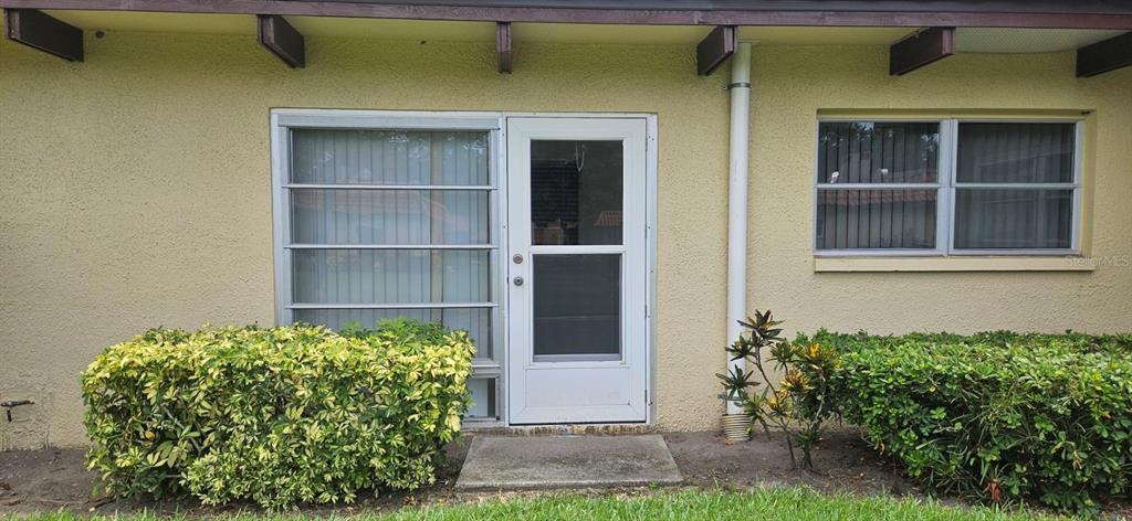 A beige stucco exterior features a central white storm door flanked by two windows — 1701 PINEHURST ROAD UNIT 16D, DUNEDIN, FL