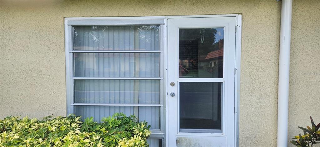 A white-framed door and a horizontal sliding window are set into a beige stucco wall — 1701 PINEHURST ROAD UNIT 16D, DUNEDIN, FL