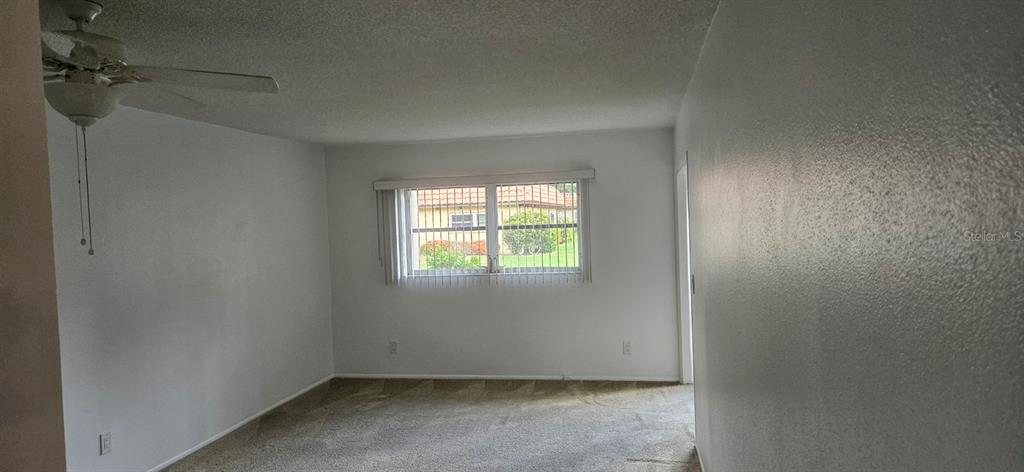 An empty room with beige carpet, white walls, a ceiling fan, and a window — 1701 PINEHURST ROAD UNIT 16D, DUNEDIN, FL