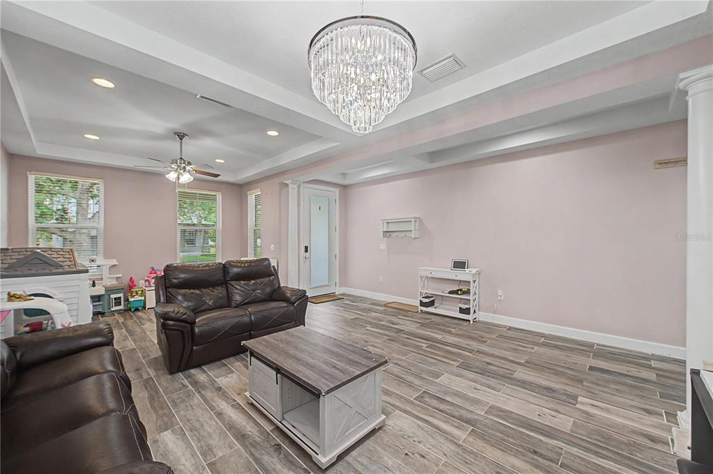 A living room features light pink walls, wood-look tile flooring, a crystal chandelier, and furniture — 8137 LAGERFELD DRIVE, LAND O LAKES, FL