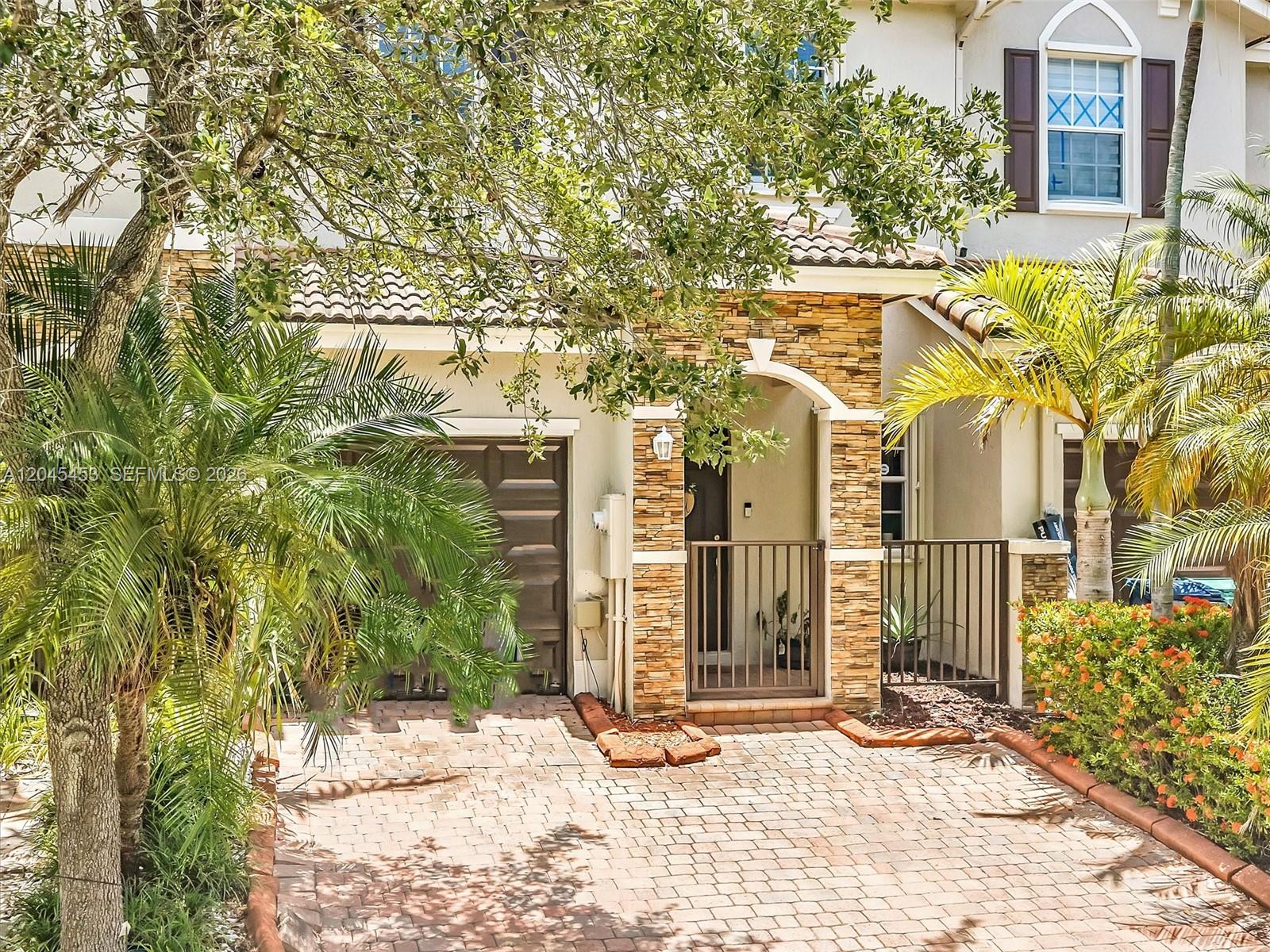 A two-story townhouse features a stone-accented entryway, a brown garage door, and a brick driveway — 8887 SW 225th St, Cutler Bay FL 33190, CUTLER BAY, FL