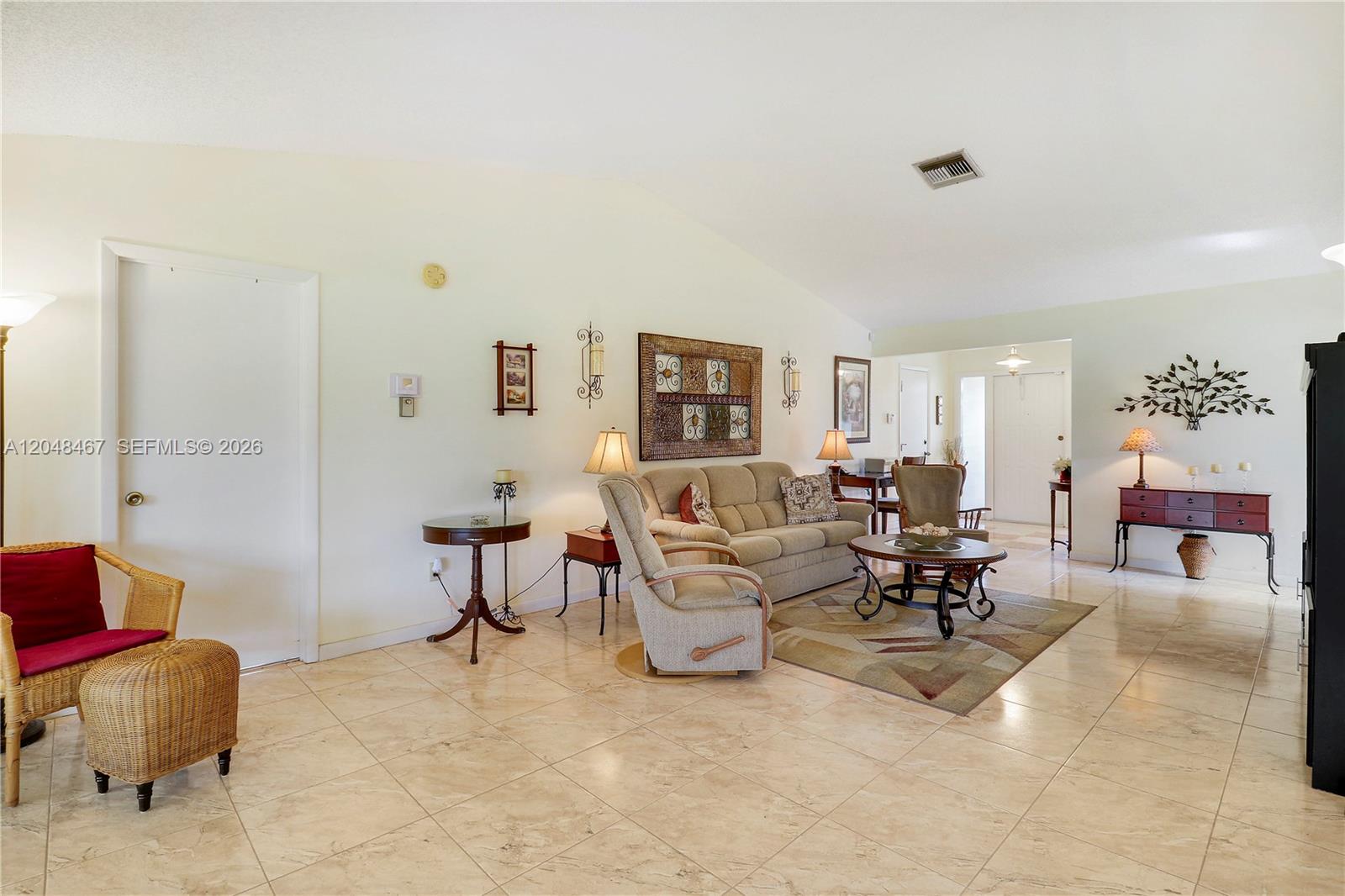 A living room features beige tile floors, a neutral sofa, and a wicker armchair — 3449 Shadow Wood Dr, Green Acres FL 33463, GREEN ACRES, FL