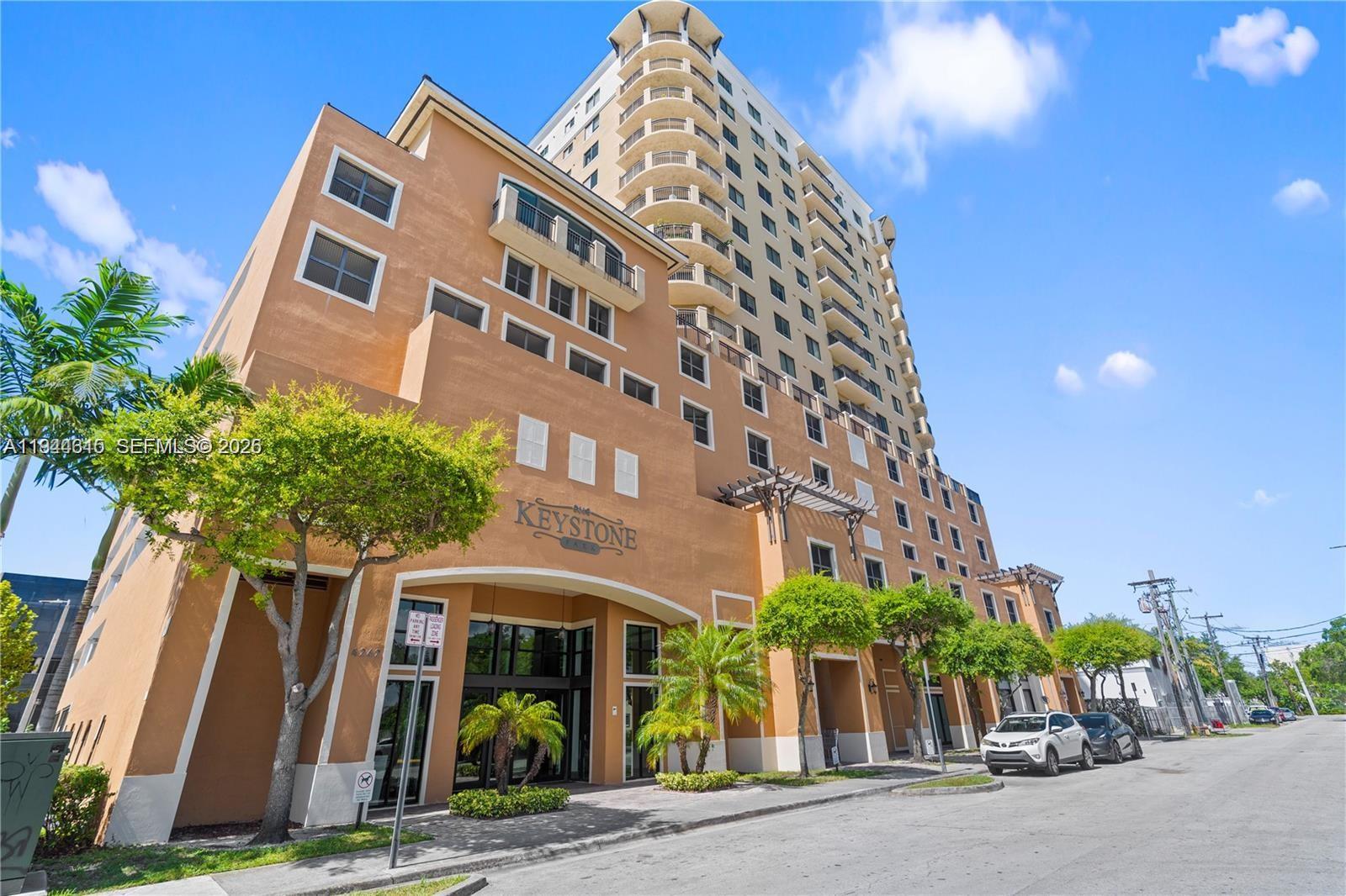 A multi-story tan apartment building features a prominent arched entrance and balconies under a blue sky — 4242 NW 2nd St # 1609, Miami FL 33126, MIAMI, FL