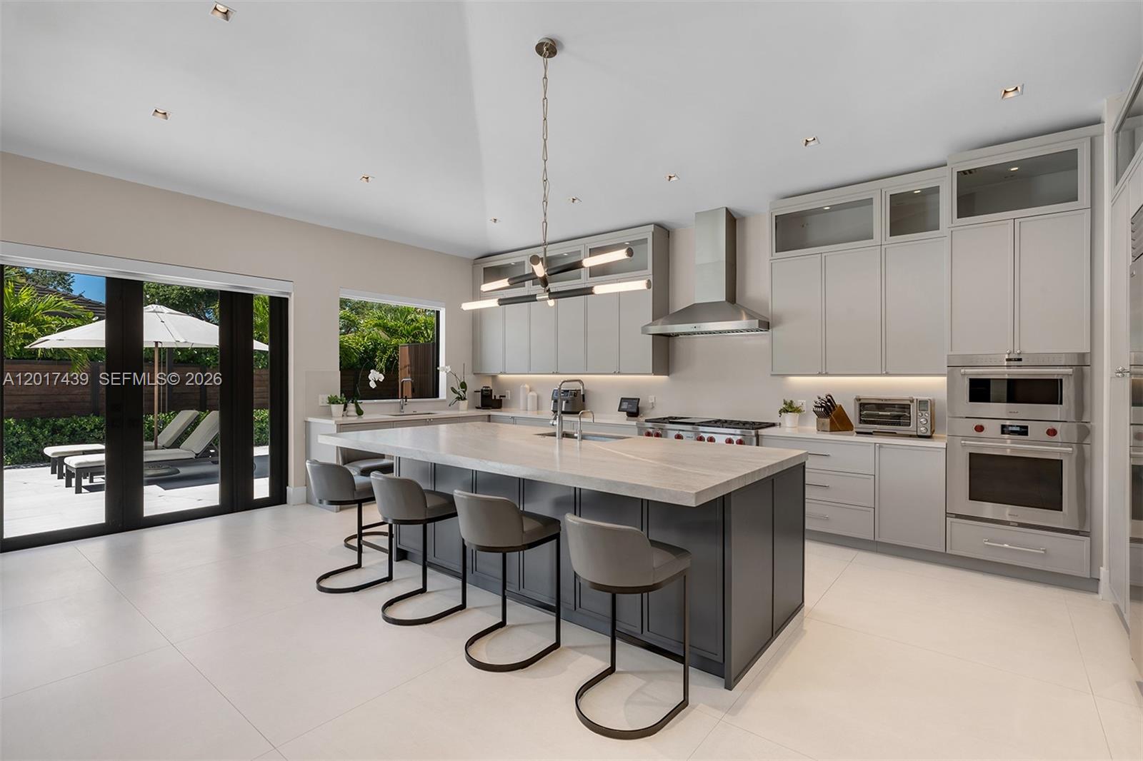A modern kitchen features a dark gray island, light gray cabinetry, and sliding glass patio doors — 10040 SW 124th St, Miami FL 33176, MIAMI, FL