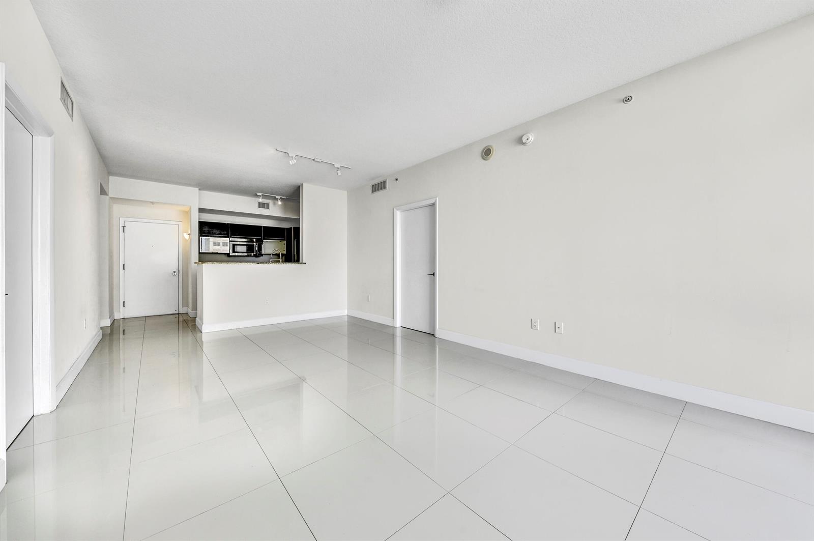 An empty living area with white tile floors, white walls, and an open kitchen — 550 Okeechobee Boulevard # 1404, West Palm Beach FL 33401, WEST PALM BEACH, FL