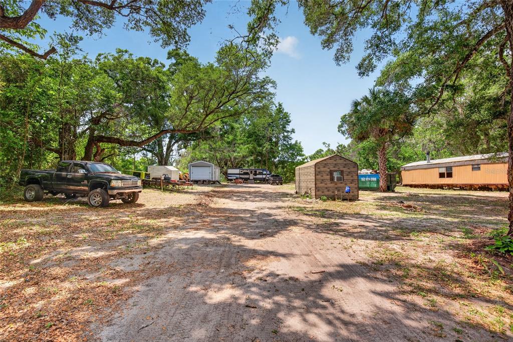 A dirt driveway leads past a pickup truck, a shed, and a mobile home outdoors — 17684 NE 24TH AVENUE, CITRA, FL
