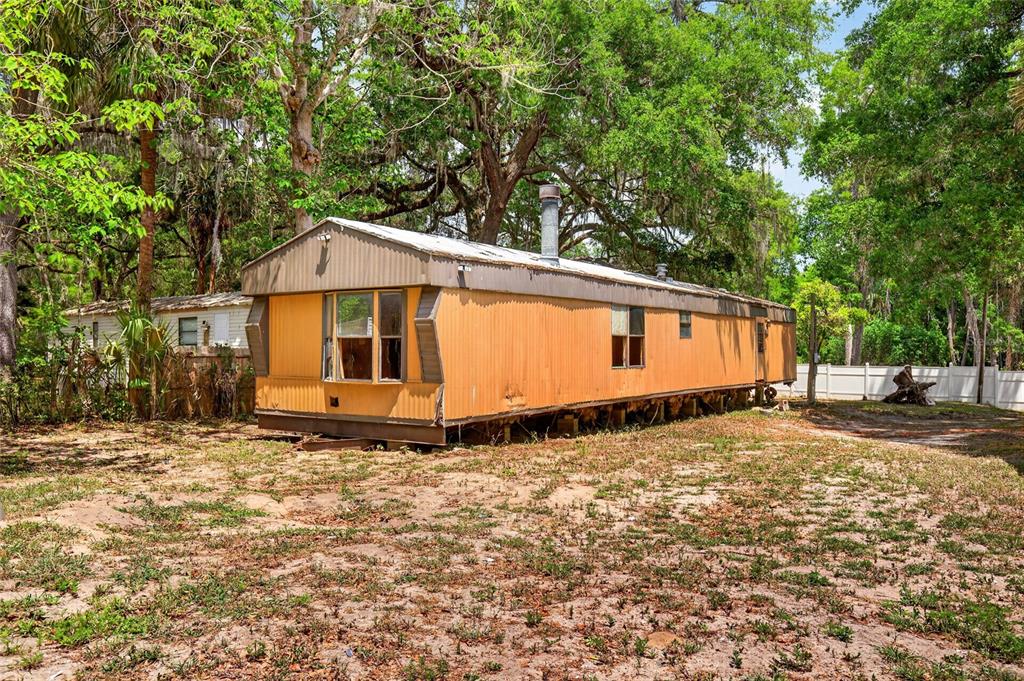 An orange mobile home sits on a dirt lot surrounded by trees and a fence — 17684 NE 24TH AVENUE, CITRA, FL