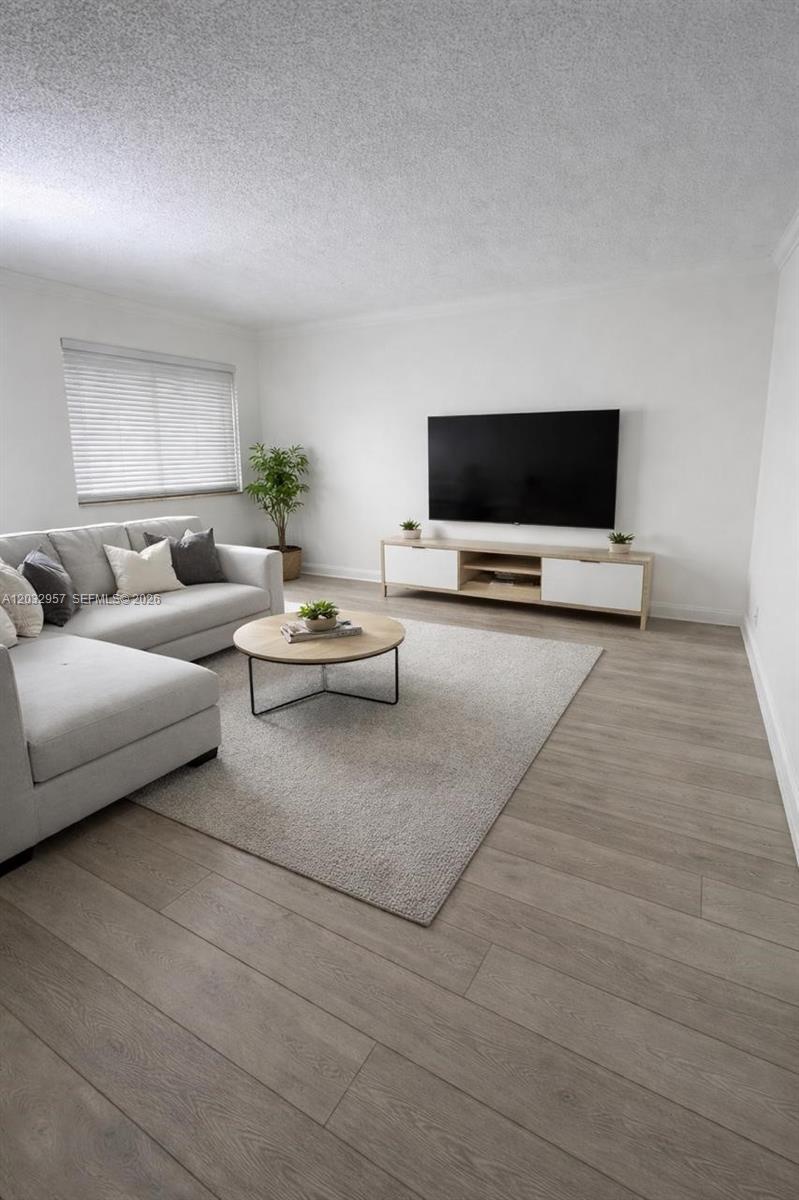 A living room features light wood flooring, a gray sectional sofa, and a wall-mounted television — 2008 N Jackson St # B4, Hollywood FL 33020, HOLLYWOOD, FL