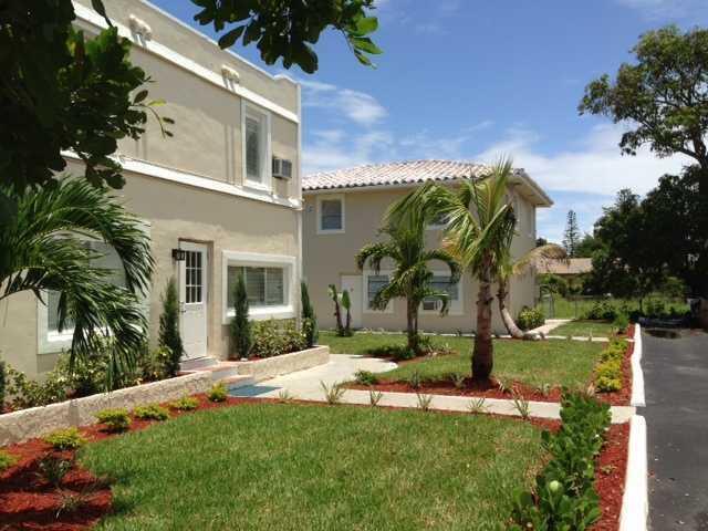 Two beige two-story apartment buildings stand on a grassy lot with palm trees and landscaping — HOLLYWOOD, FL