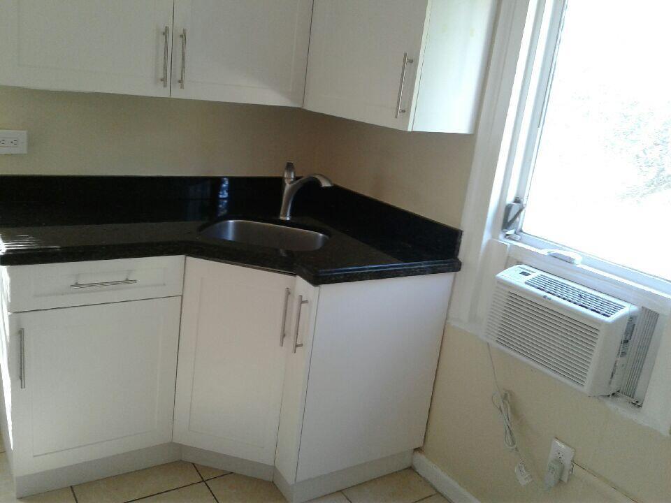 A kitchen corner features white cabinets, a dark granite countertop, a sink, and a window unit — HOLLYWOOD, FL