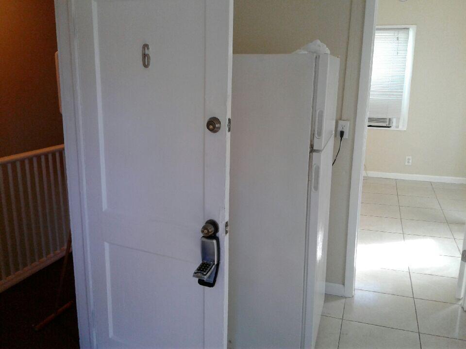 A white door with a keypad lock opens into a room with a white refrigerator — HOLLYWOOD, FL