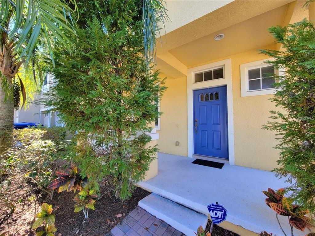 A bright blue front door sits under a covered porch with yellow exterior walls — 9722 MOSS ROSE WAY, ORLANDO, FL