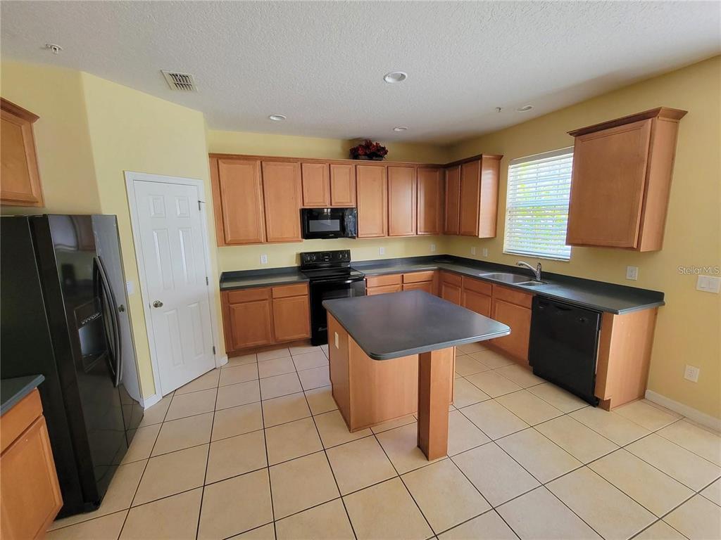 A kitchen features light wood cabinets, dark countertops, black appliances, and a central island — 9722 MOSS ROSE WAY, ORLANDO, FL