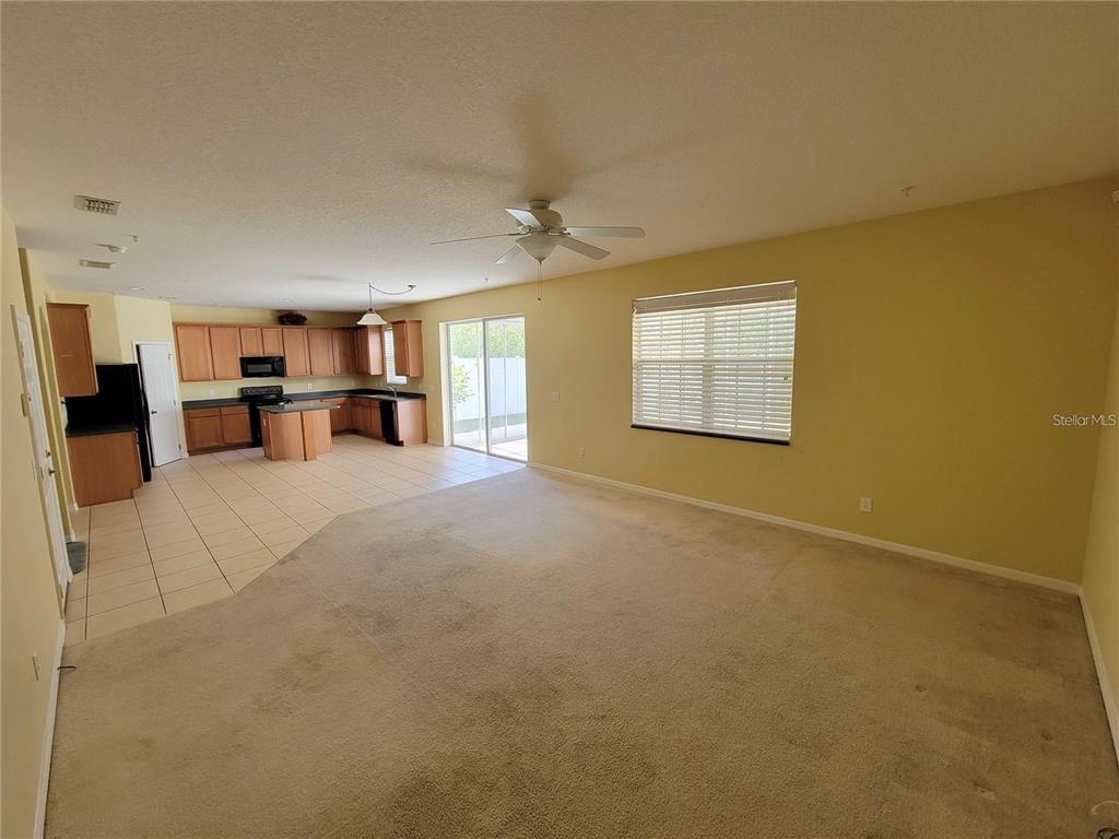 An open-concept living room with beige carpet flows into a kitchen with tile flooring — 9722 MOSS ROSE WAY, ORLANDO, FL