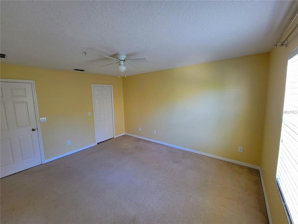 An empty bedroom features yellow walls, beige carpeting, a ceiling fan, and two white doors — 9722 MOSS ROSE WAY, ORLANDO, FL